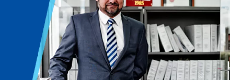 Man in a suit standing in an office with shelves of binders.