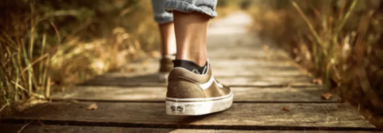 Person walking on a wooden path in nature, wearing casual sneakers and jeans.