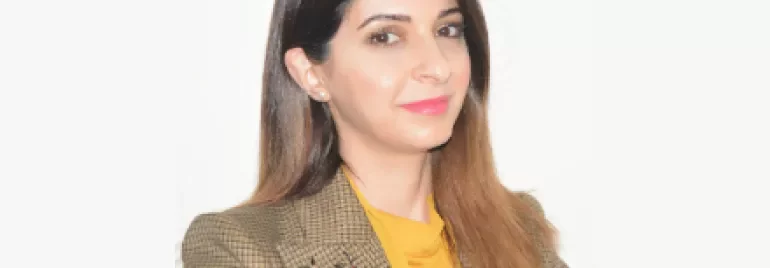 Portrait of a woman in a yellow top and patterned blazer, smiling.