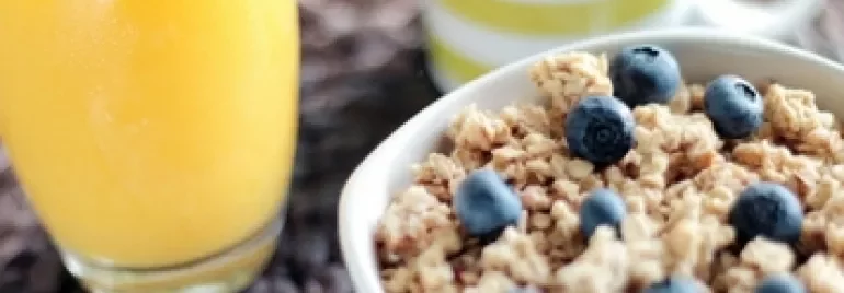 Bowl of granola with blueberries next to a glass of orange juice and a striped mug.