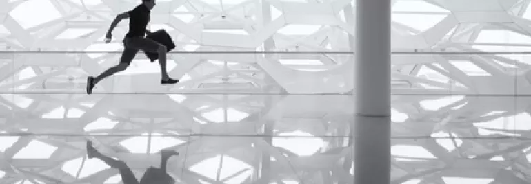 Silhouette of a man running indoors with a patterned wall reflection on the shiny floor.