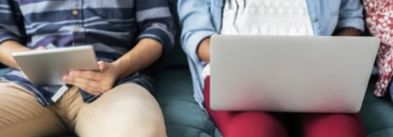 Two people sitting on a sofa with a tablet and a laptop.