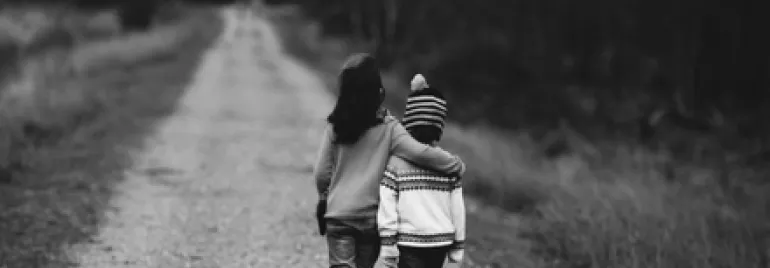 Two children walking on a rural path, one with an arm around the other, in black and white.