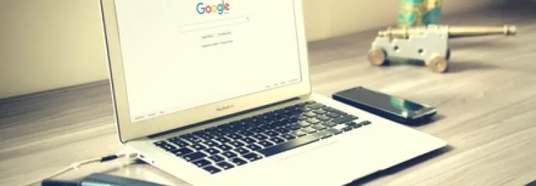 Laptop with Google search on screen, placed on a desk with a phone and notebook.