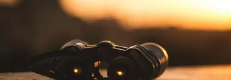 Binoculars on a ledge at sunset with a blurred background.