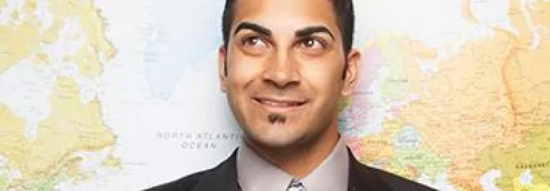 Smiling man in a suit stands in front of a world map.