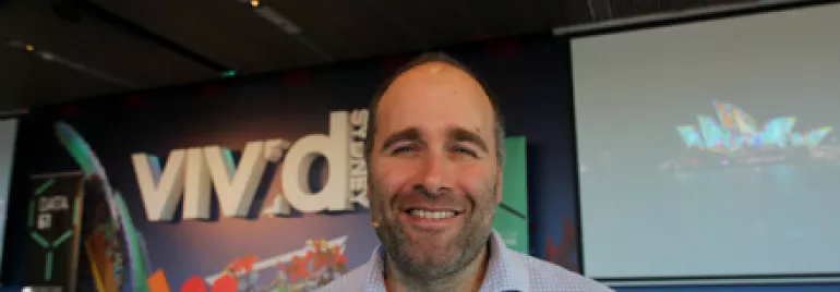 Smiling person in front of Vivid Sydney poster with colorful design elements.