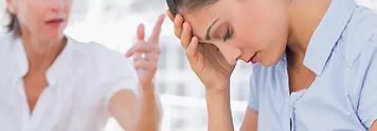 A woman sits with her head in her hand while another woman speaks to her in the background.