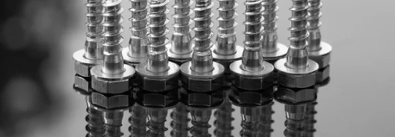 Nine shiny metal screws standing upright on a reflective surface.