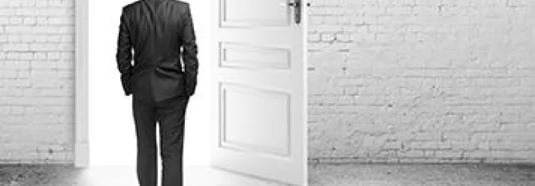 Man in a suit walking through an open door into a bright space.