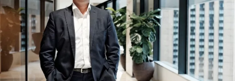 Smiling man in a suit standing in a bright office hallway.