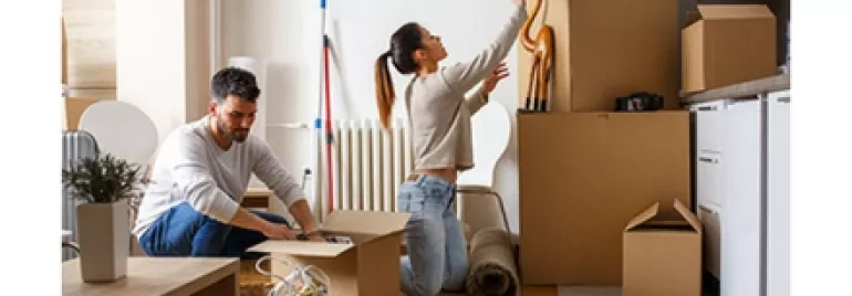 A couple unpacking boxes in a room with wooden floors.