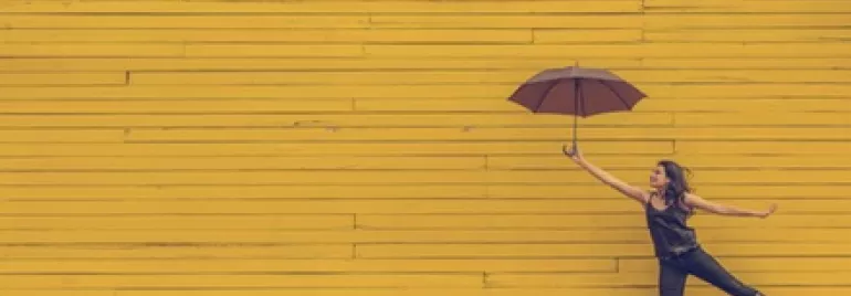 Person holding an umbrella and jumping against a yellow wooden wall.