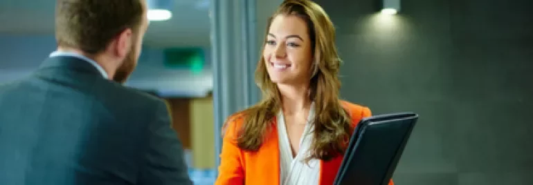 Woman in orange blazer shakes hands, holding a folder.