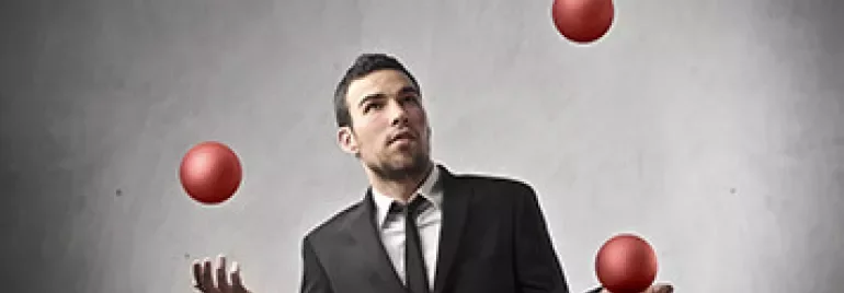 Man in a suit juggling four red balls with a focused expression.