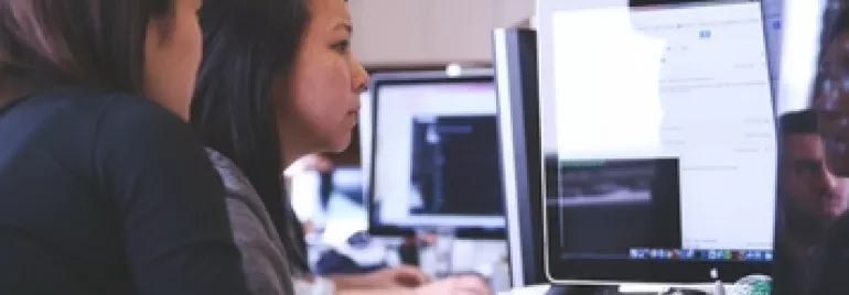 Two women collaborating at a computer in an office setting.
