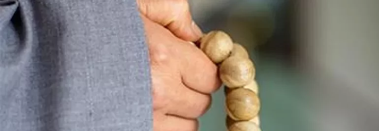 Person in gray robe holding wooden prayer beads.