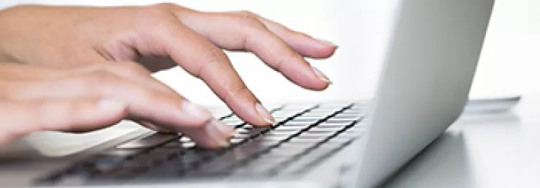 Person typing on a laptop keyboard with white background.