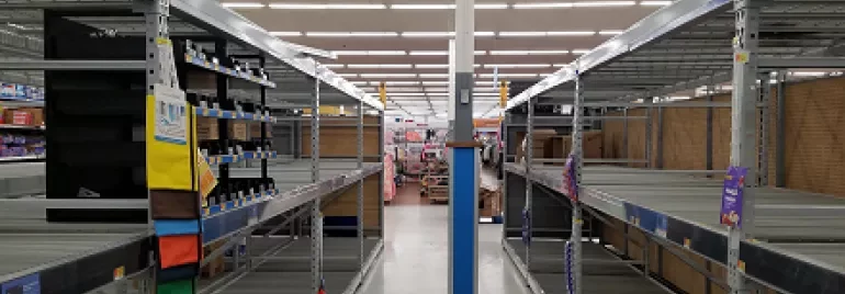 Empty store shelves with sparse items, wide aisle in a supermarket.