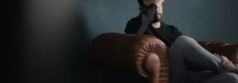 Man sitting on a leather couch with his hand on his face, looking tired.