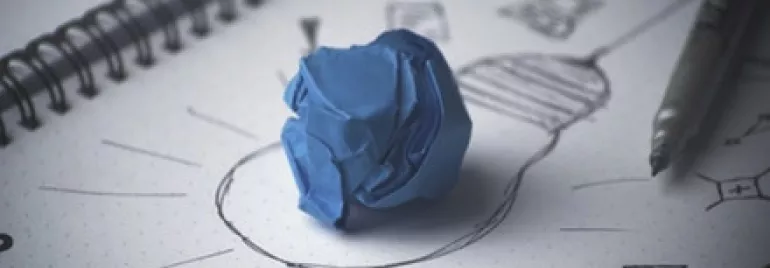Sketch of light bulb with crumpled blue paper on notepad.