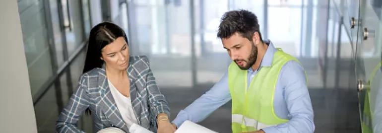 Two people discussing blueprints in a modern office stairwell.