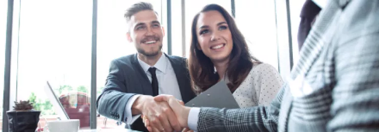 Business meeting with three people, two shaking hands, one smiling.