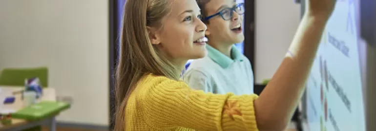 Two students using a smartboard in a classroom, engaging in an interactive lesson.