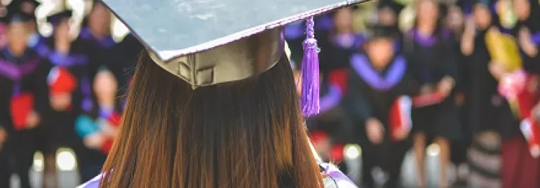 Graduate in cap and gown facing a group of fellow graduates.