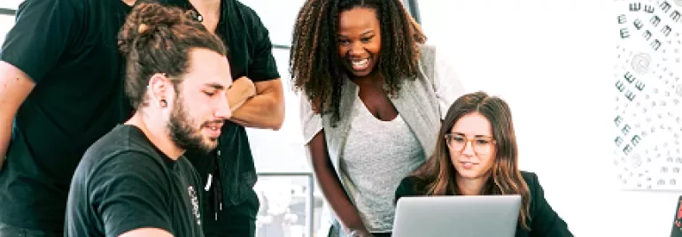 Group of people collaborating around a laptop in a bright office.