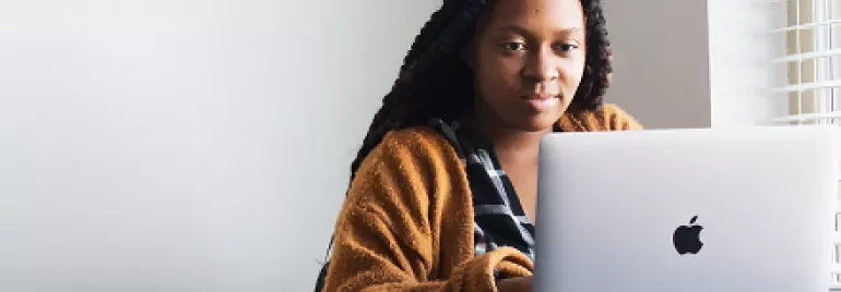 Person in a brown sweater using a laptop at a desk.