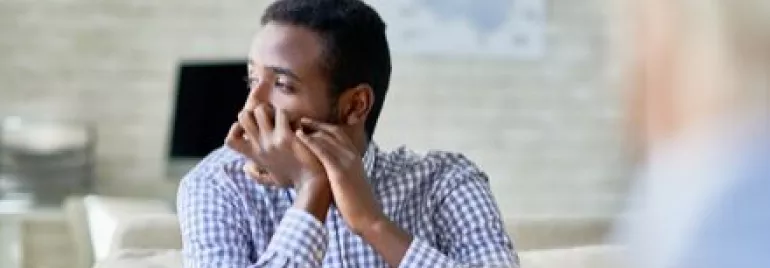 Man in a checkered shirt looking pensive in a bright room.