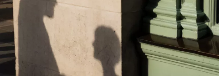 Silhouettes of two people in conversation cast on a wall beside a green building column.
