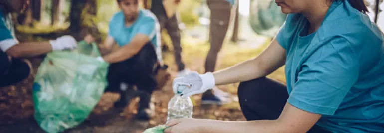 Volunteers in blue shirts and caps picking up litter in a forested area.