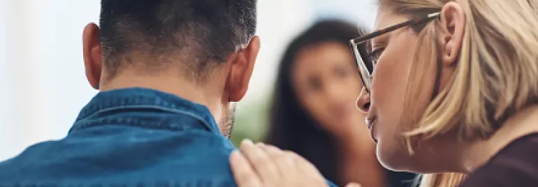 Woman comforting a man, placing her hand on his shoulder.