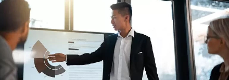Person giving a presentation with charts on a screen in a meeting room.
