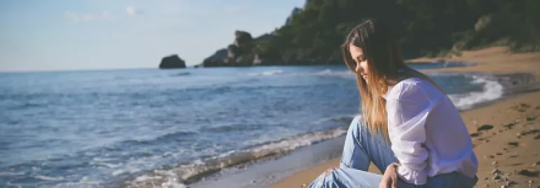 Woman sitting on a sunny beach, gazing at the ocean.