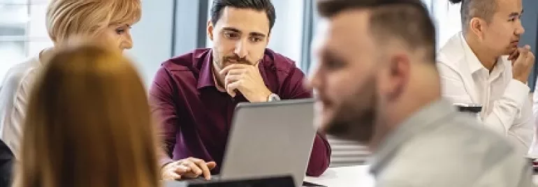 A group of people having a meeting around a table with laptops.