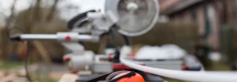Orange ear protection and a saw on a workbench in a backyard setting.