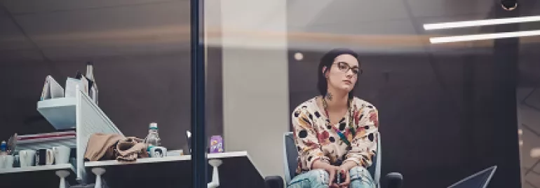 Woman in a patterned shirt sitting by a window in an office.