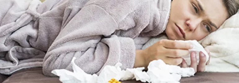 Woman in bathrobe lying on a couch surrounded by tissues and medicine packs.