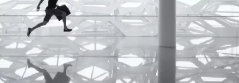 Silhouette of man running with a briefcase against geometric wall, reflected on shiny floor.