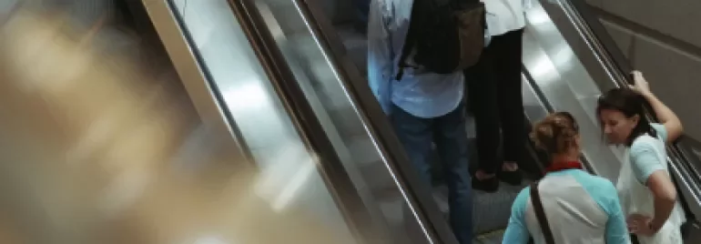 People going up and down on parallel escalators in a busy station.