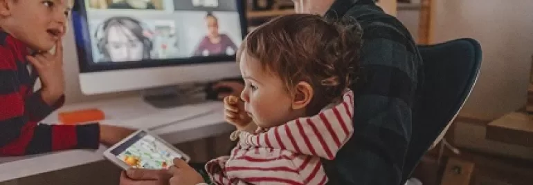 Parent working from home with children nearby during a video call.
