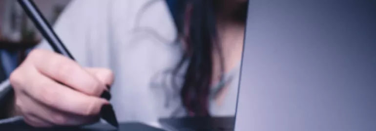 Person using a stylus on a tablet next to an open laptop.