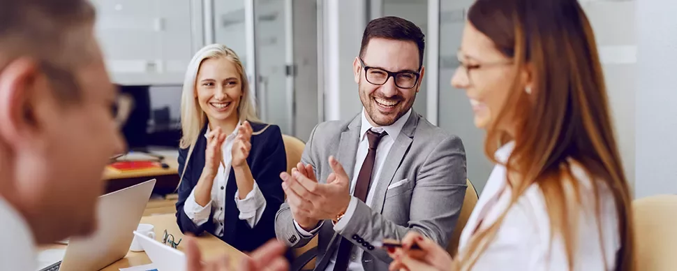 Group of professionals smiling and clapping in a modern office meeting.