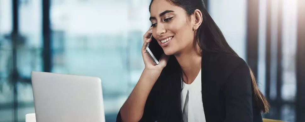 Woman in an office talking on the phone while using a laptop.