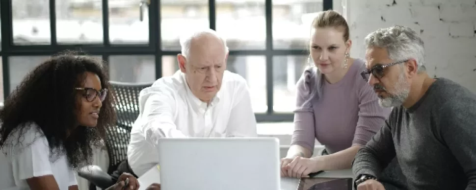 Group of four people collaborating around a laptop in a bright room.