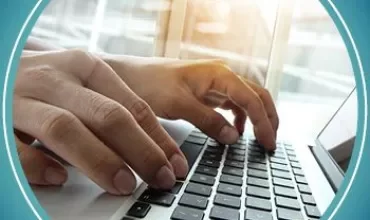 Hands typing on a laptop keyboard with sunlight in the background.
