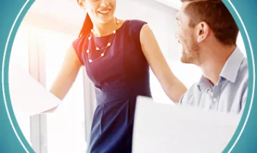 Woman in blue dress smiling while talking with a man in an office setting.